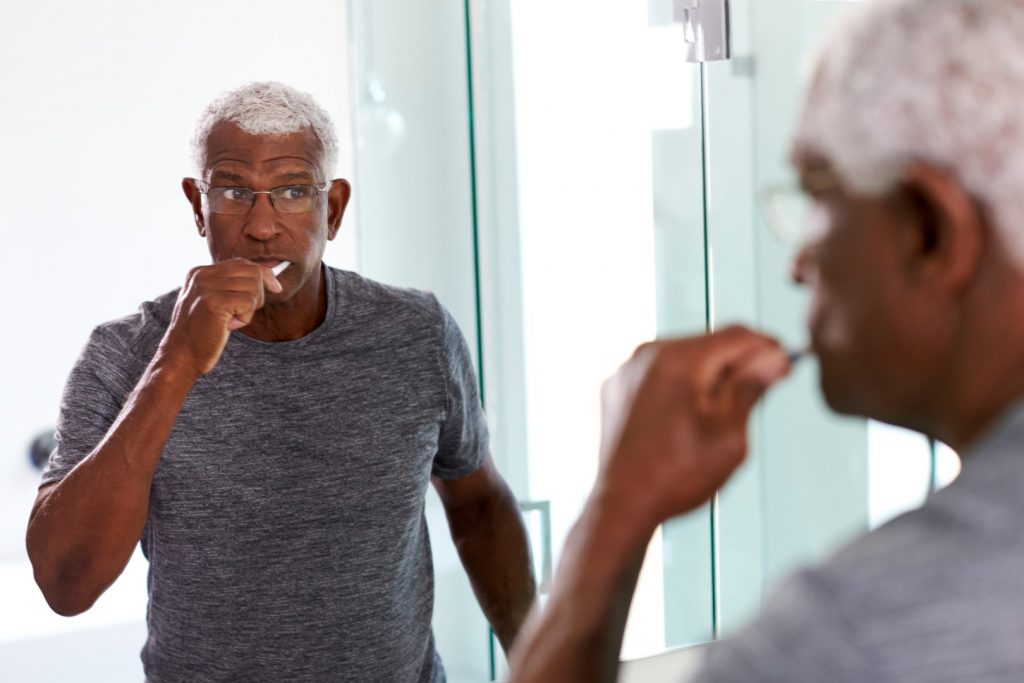 A man stands in front of a bathroom mirror, using proper tooth brushing techniques to help treat his tooth sensitivity. 