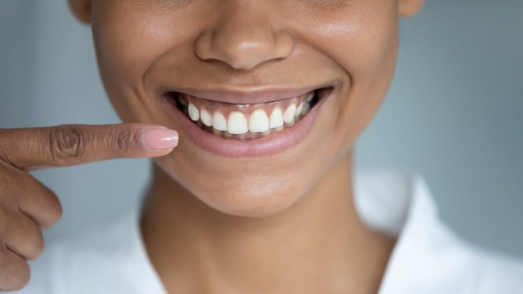 A woman smiles and points to her healthy gums after receiving treatment from an expert, low-cost periodontist in Philadelphia.