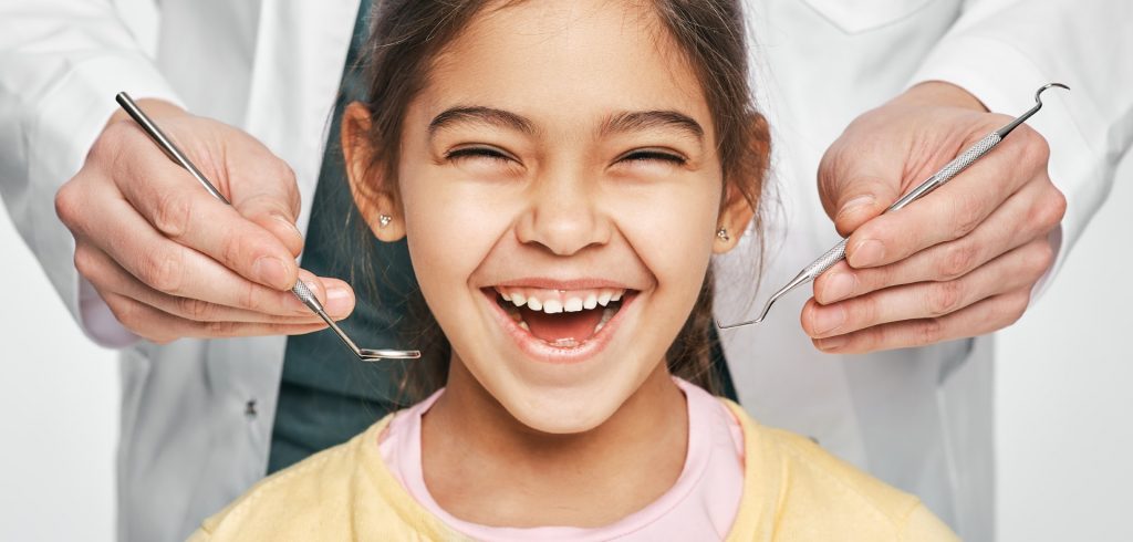 A young girl smiles with healthy summertime teeth as she visits her dentist before she goes back to school. 