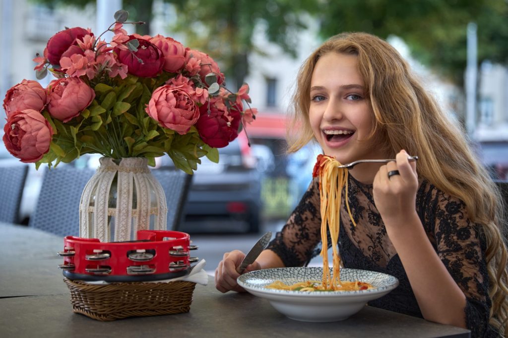 A high-school-age girl sits outdoors at a restaurant eating spaghetti, a good example of what you can eat with braces.