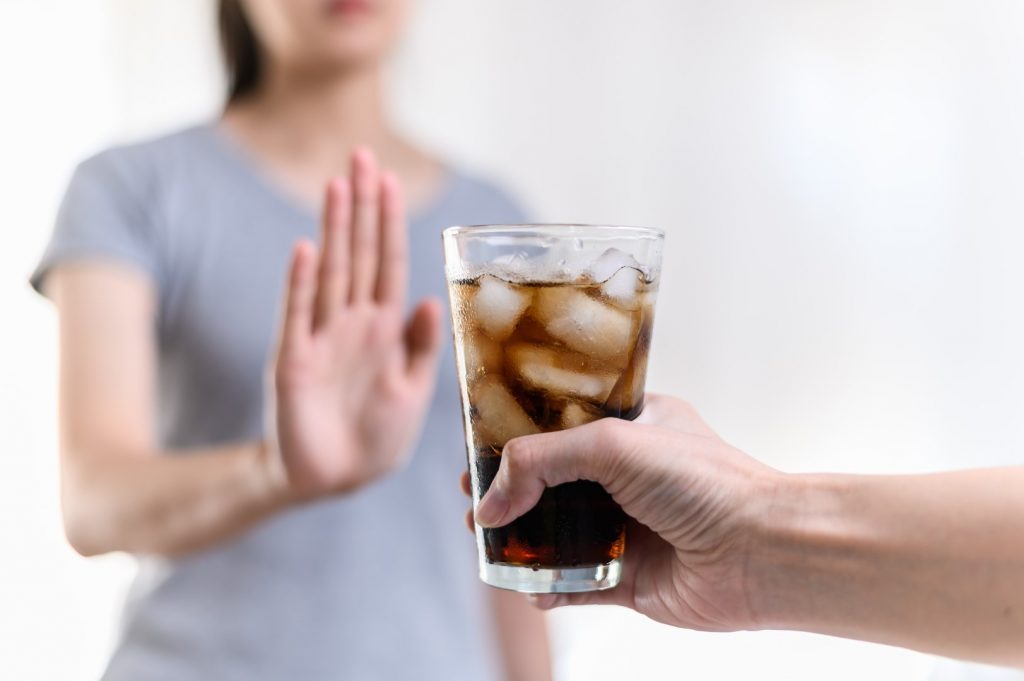 A woman holds out her hand to say no to a sugary soda that could hurt her summertime teeth.