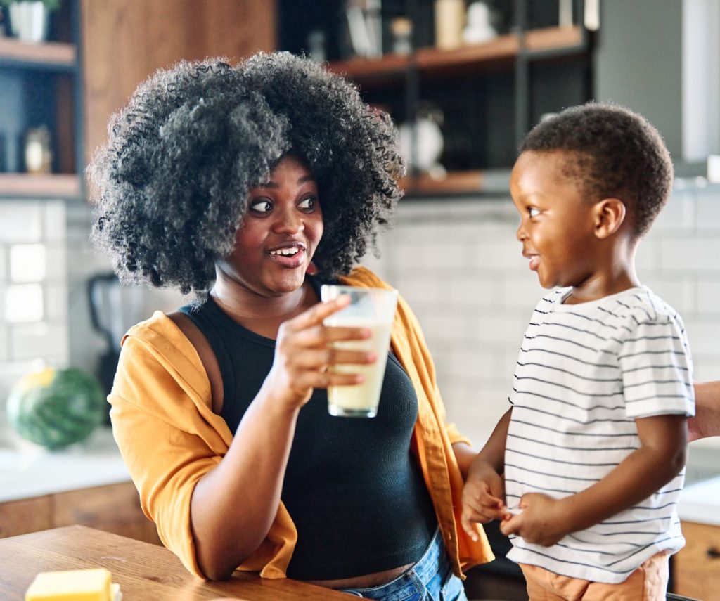 A mother smiles as she drinks milk, one of the best drinks for good nutrition and oral health, with her smiling toddler son.