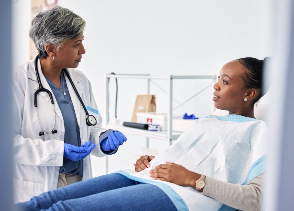 A woman reclining in a dental chair asks her dentist, “Why are my teeth sensitive?”