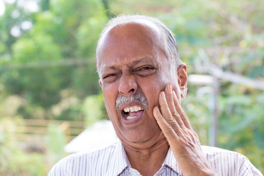 An older man grimaces with his hand to his mouth, needing dental care for seniors.