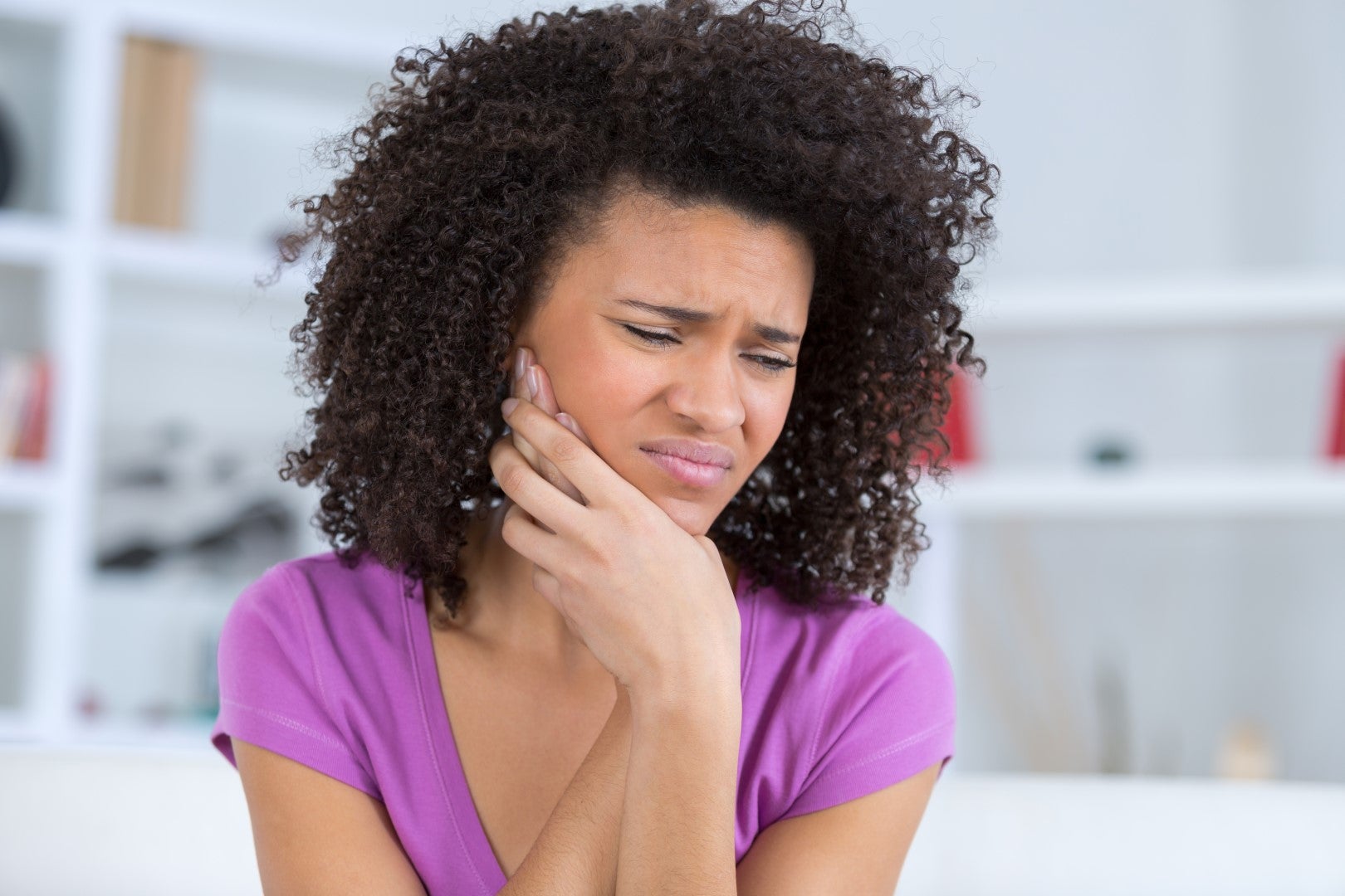 A young woman frowns and holds her hand to her sore mouth as she wonders, “How long does a toothache last?”