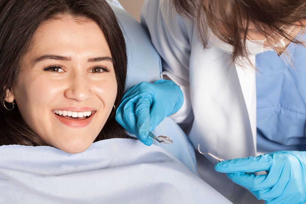 A woman reclining in a dental chair smiles as an affordable prosthodontist in Philadelphia completes placing a dental crown.
