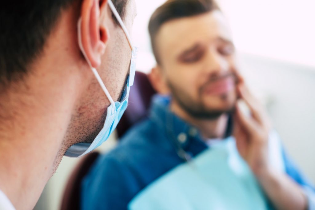 A man holds his hand to his jaw as the dentist explains periodontitis treatment options.