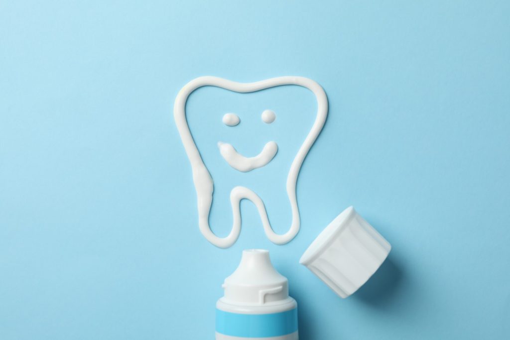 An illustration of a smiling tooth with a toothpaste tube and cap next to it. 