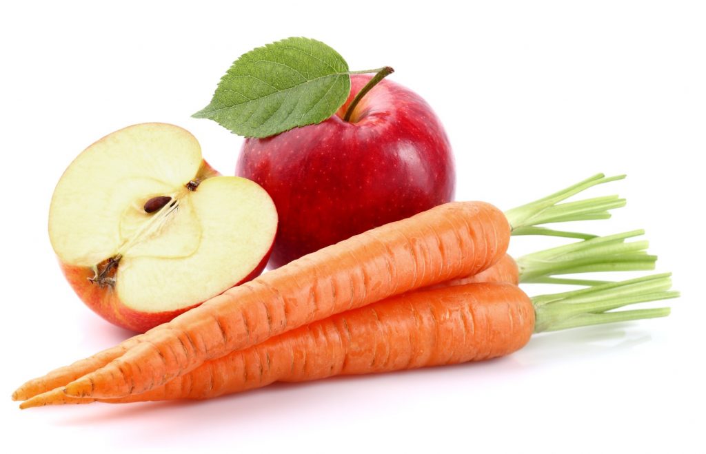 Three fresh carrots are on the counter next to one whole fresh apple and one half of a fresh apple.