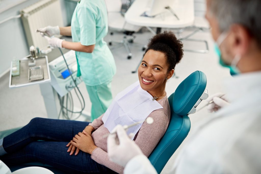 A woman reclining in a dental chair listens to budget-friendly oral health advice from her dentist.