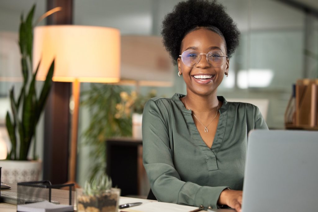 A young woman works on her laptop and smiles because she followed her dental New Year's resolutions.