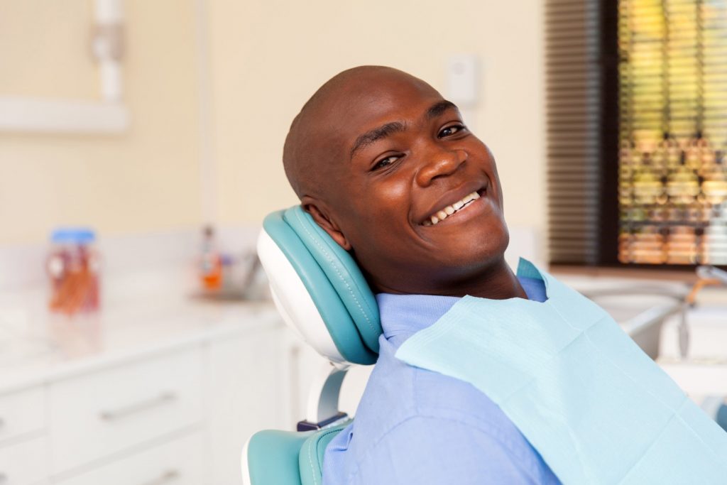 A man smiles from the dentist's office exam chair after his periodontitis treatment.