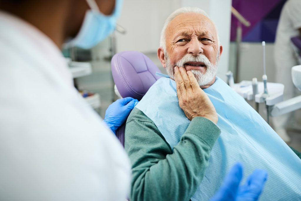 An older man holds his hand to his dry mouth as he talks to his dentist about dry mouth treatments. 