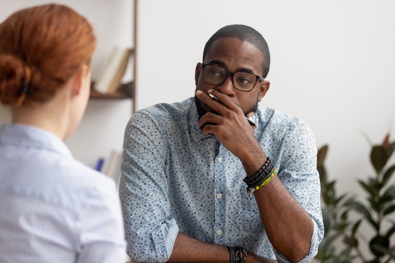 A man looks uncertain as he speaks with a health professional about his stress & dental health. 