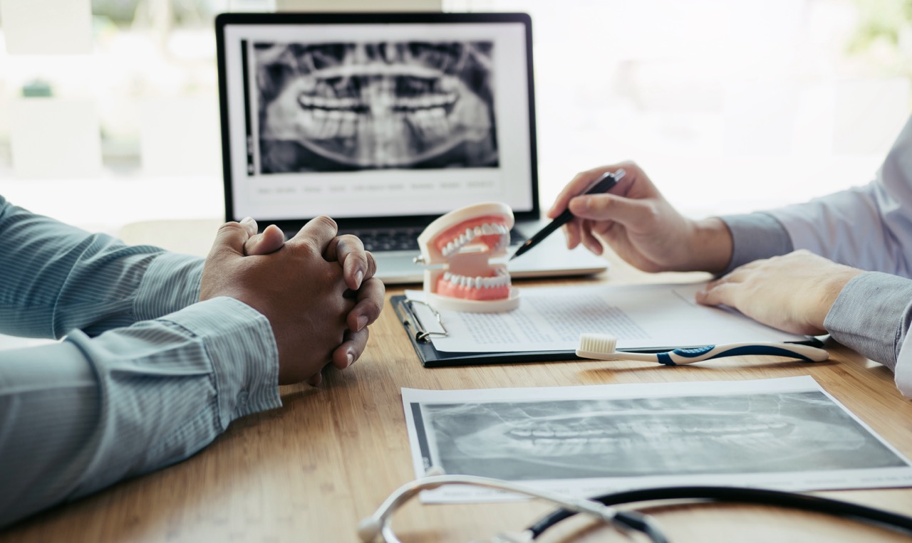 A dentist points to stress dental signs on a teeth model to a patient. 