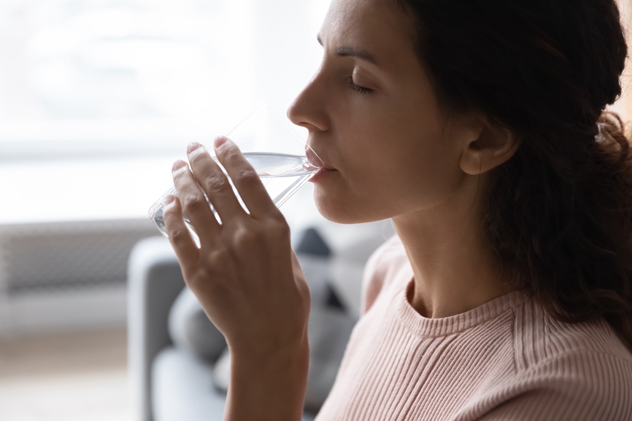 Woman sips a glass of water as part of her home care for her dry mouth (xerostomia).