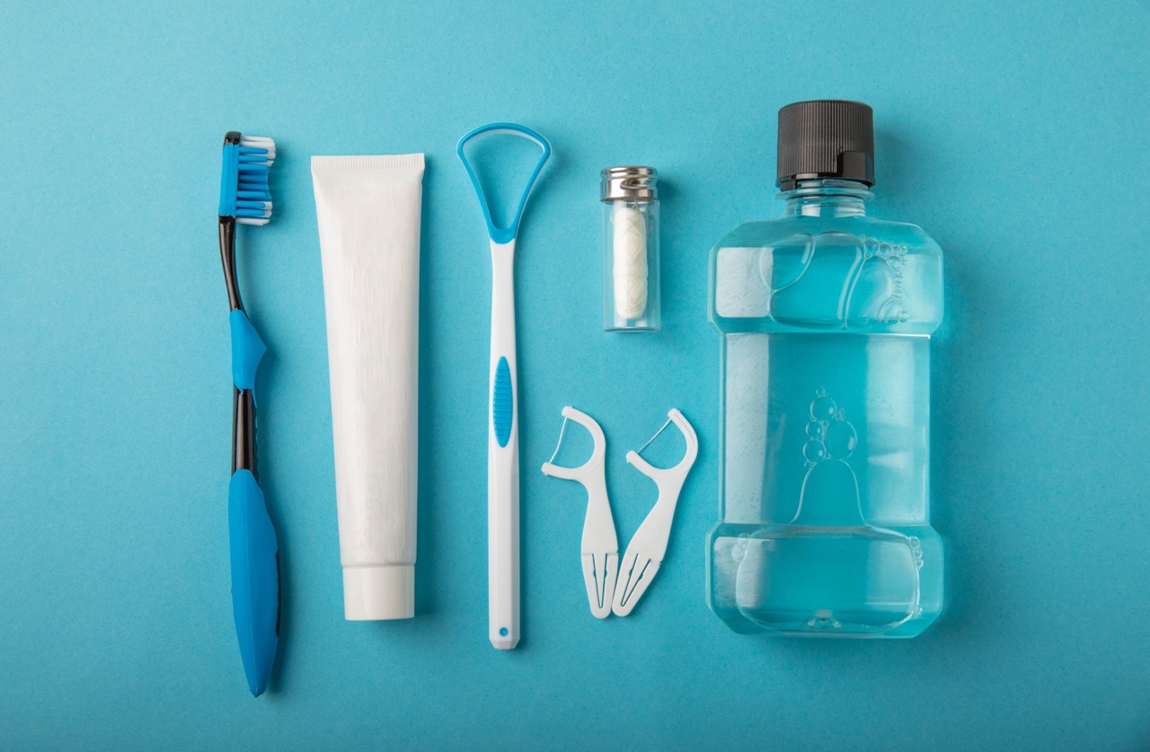 A toothbrush, tongue cleaner, floss, toothpaste tube, and mouthwash on a blue background.