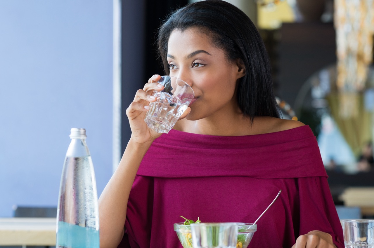 Woman drinks glass of plain water after drinking soda, to minimize the harmful effects of soda on teeth.