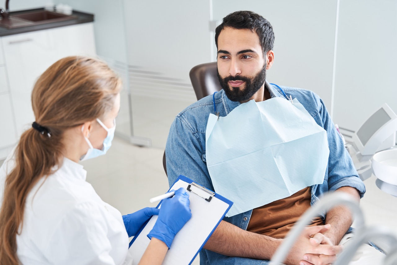 A man talks to his dental hygienist about his fear of dental procedures as she takes notes.