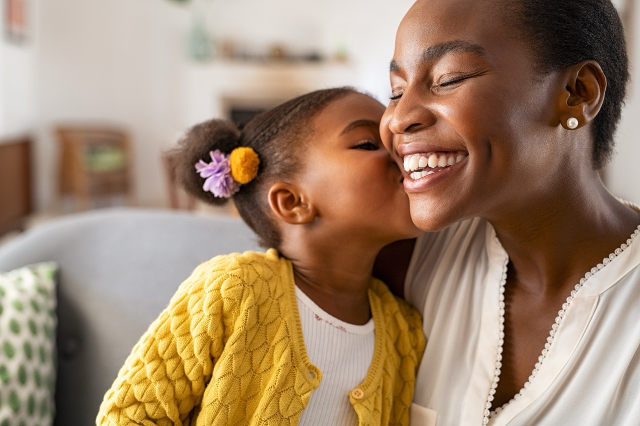 A little girl leans in to kiss her mother’s cheek. 