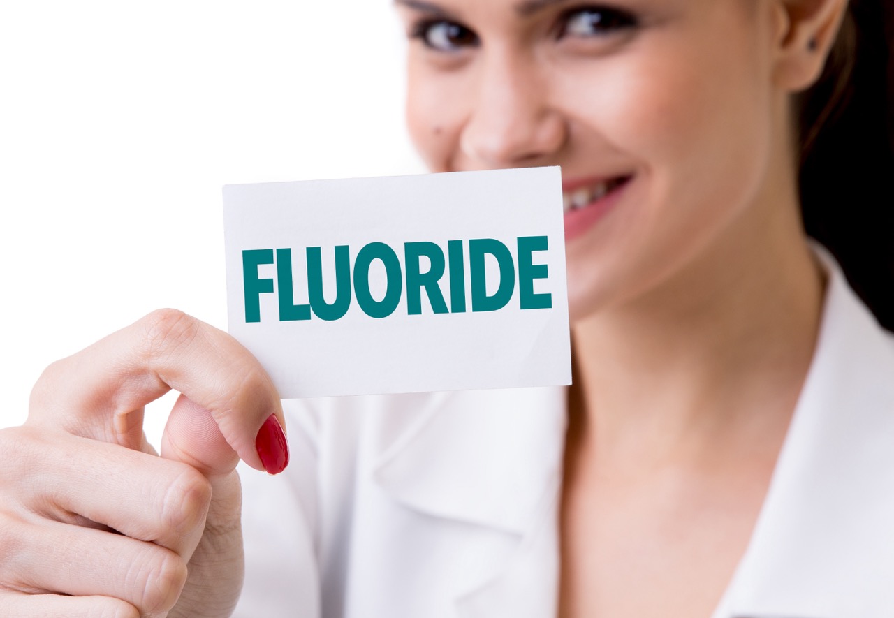 A dental hygienist holds a card that says “FLUORIDE.”