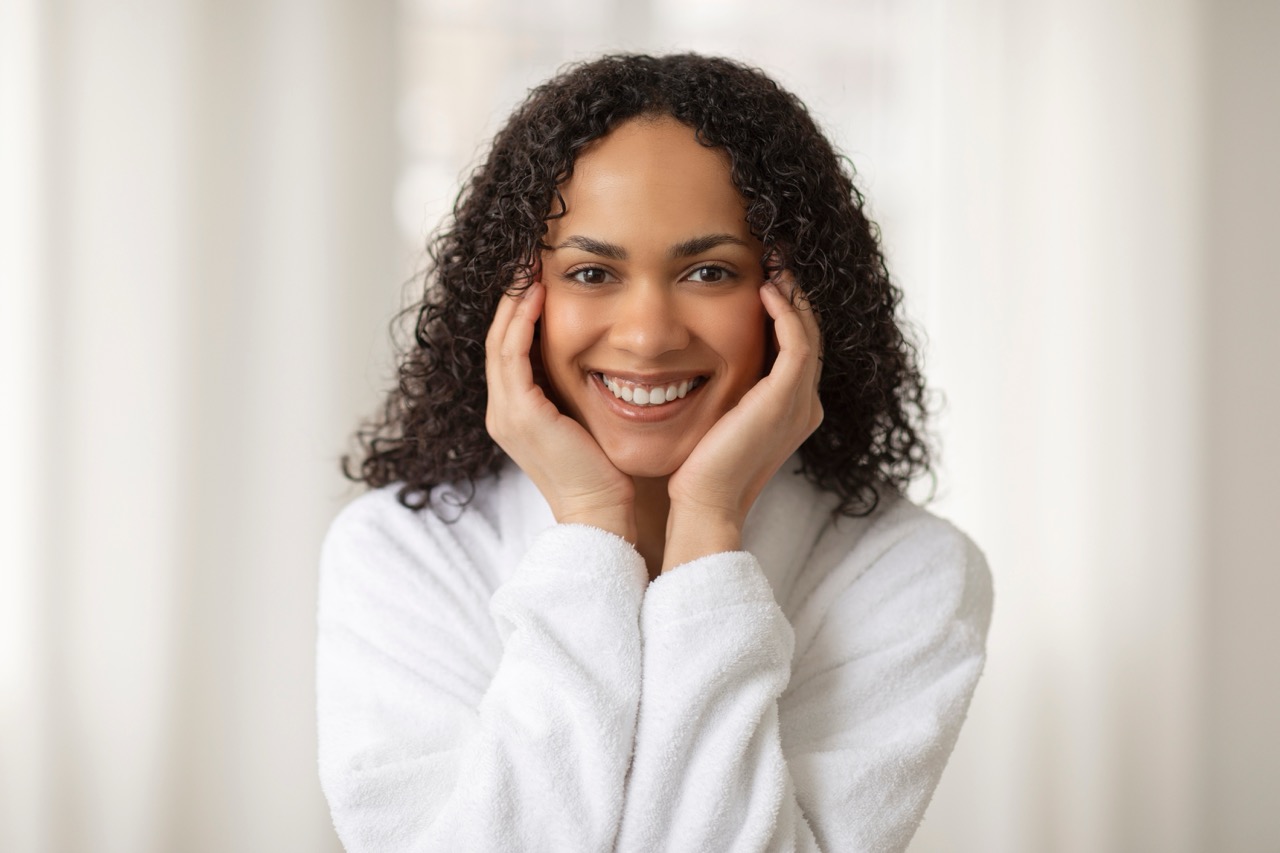 A young woman smiles as she holds her hands up to her face because she knows her diabetes and oral health are in good shape. 