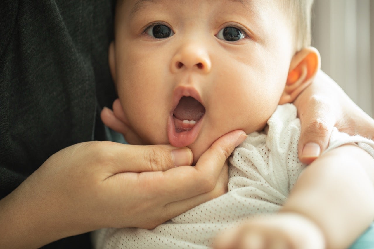 A mom holds her baby’s mouth open to show two small front teeth. 