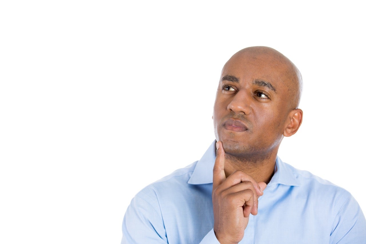A man wearing a blue shirt holds his finger to his chin as he thinks about what causes oropharyngeal cancer. 