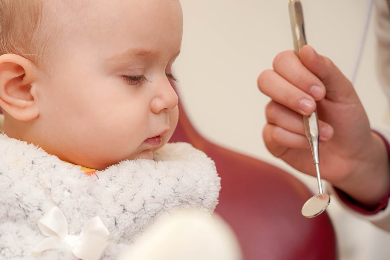 A baby looks at a mirror tool the dentist holds in front of it. 