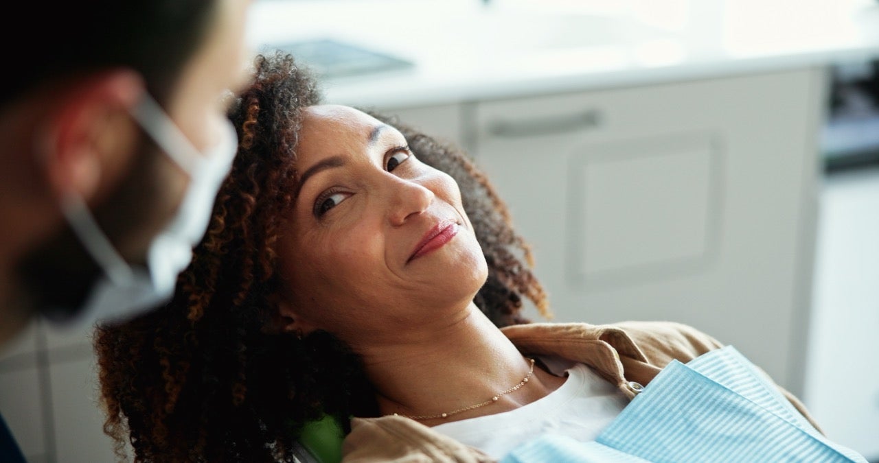 A middle-aged woman smiles at her dentist during her dental exam. 