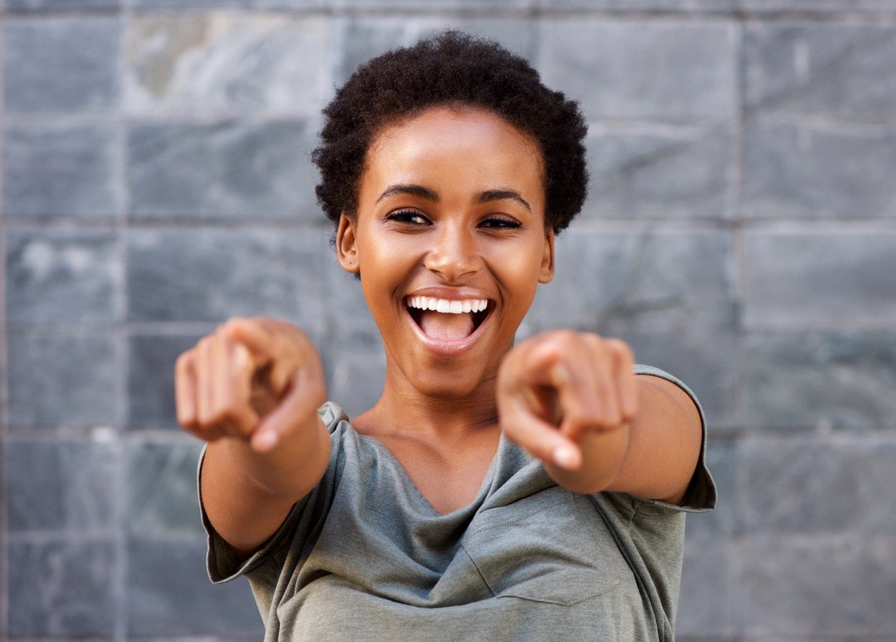 A happy young woman smiles because she is happy with her oral health and points her hands out in front in emphasis.