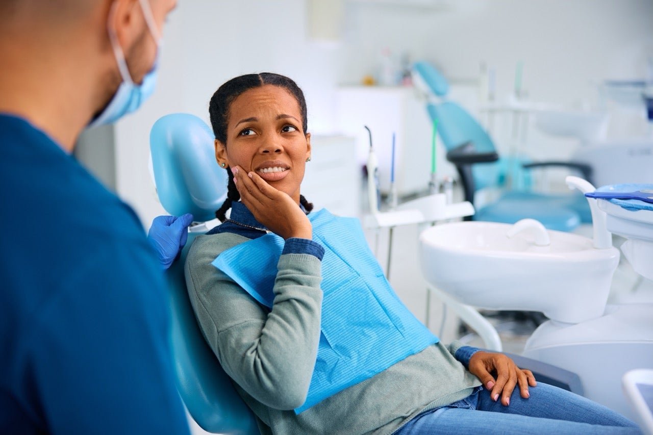 A young woman holds her hand to her mouth while she talks to the dentist. 