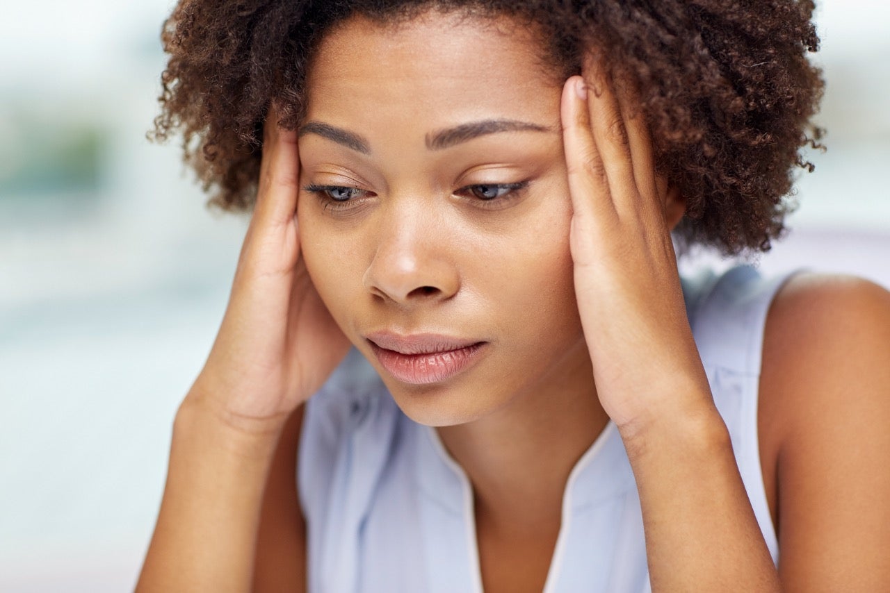 A young woman holds her hands to her temples and wonders if dental issues can cause headaches. 