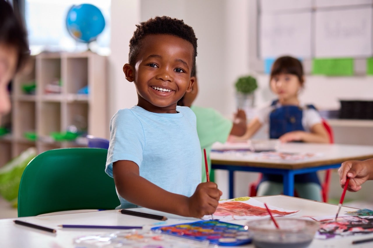 A cute little boy smiles as he colors at preschool. 