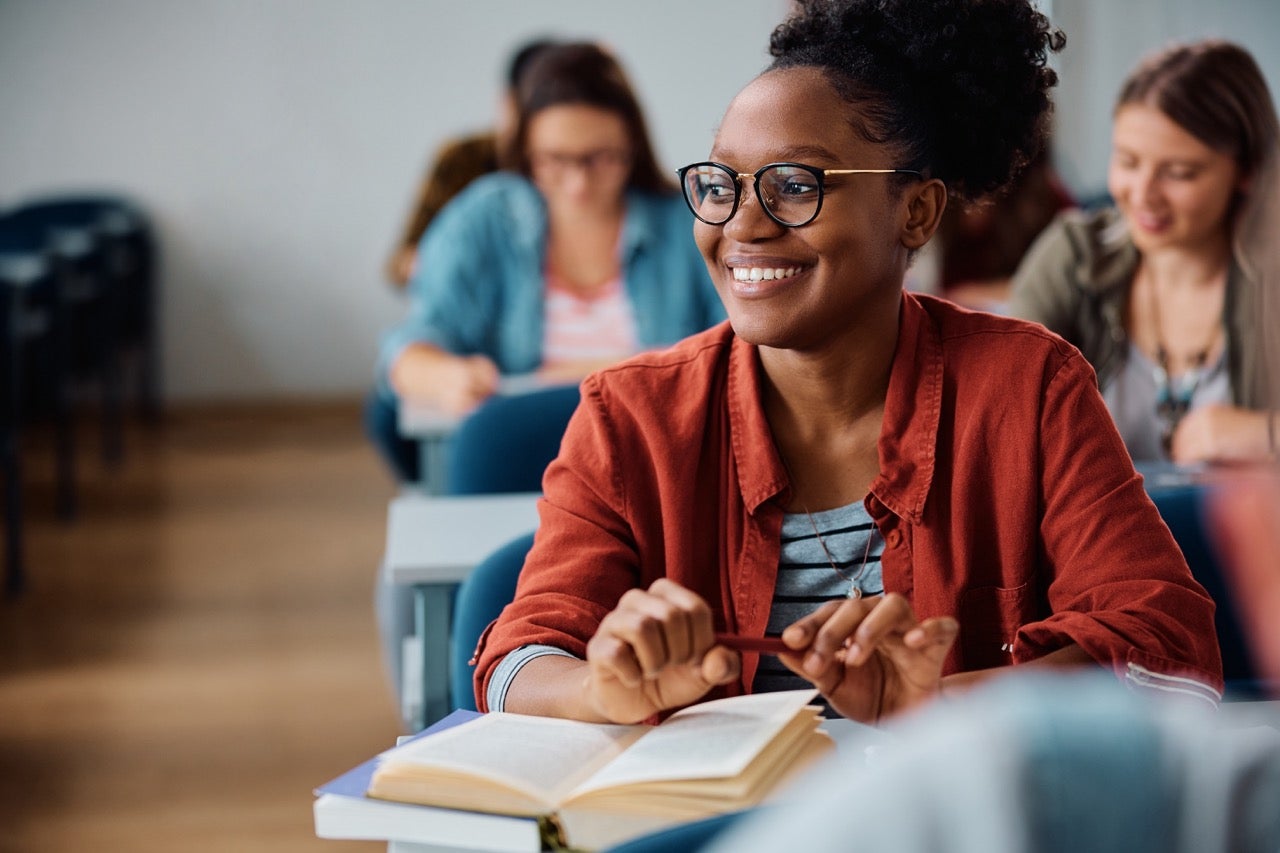 A young woman sits in a classroom and smiles because she feels better after recovering from wisdom tooth removal.