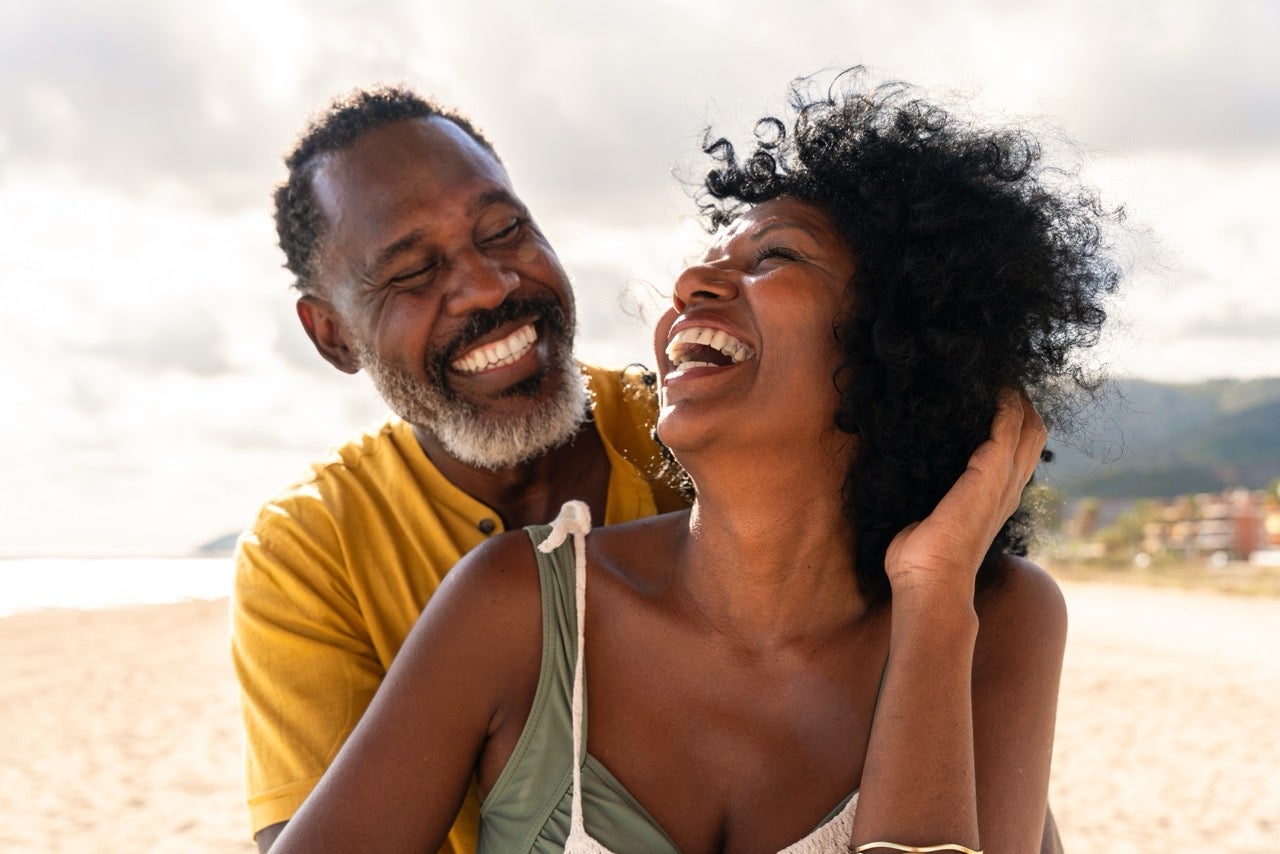 A couple standing close together at the beach smiles at each other now that their bad breath has been treated. 