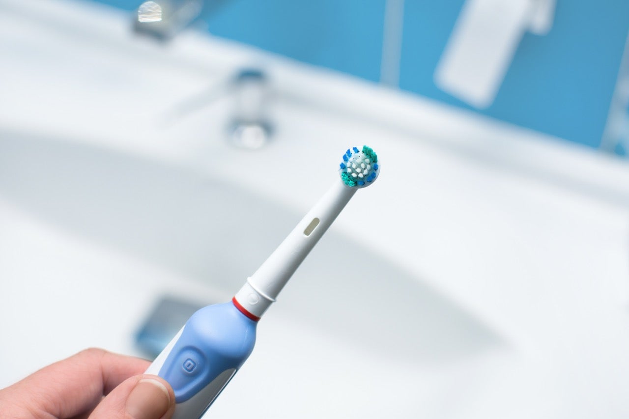 A person holding an electric toothbrush over a bathroom sink. 