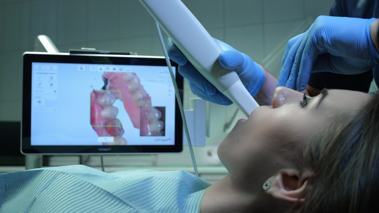 A dentist scans a patient’s teeth as an image appears on a screen. 