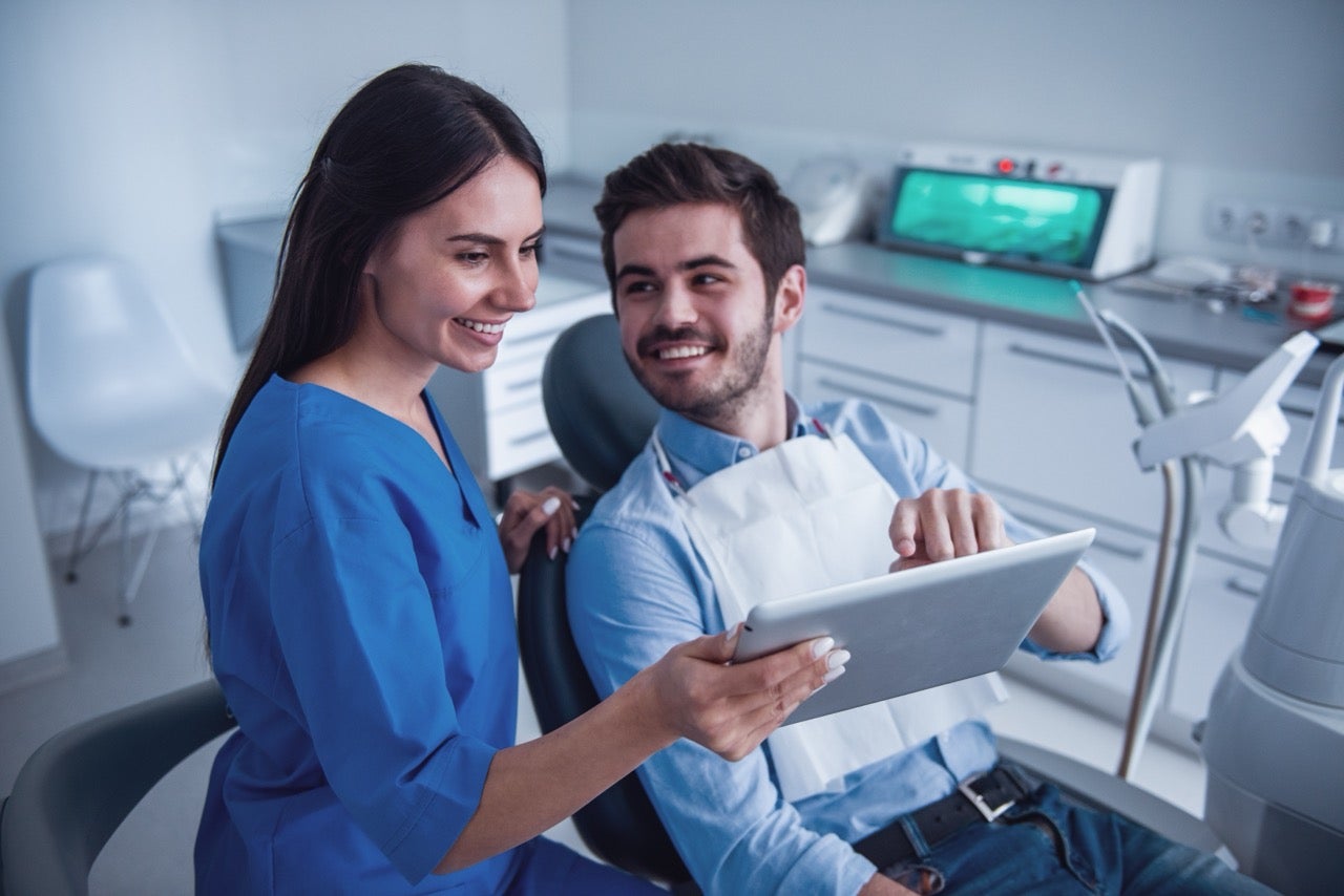 A dentist shows a male patient digital dental impressions on a tablet. 