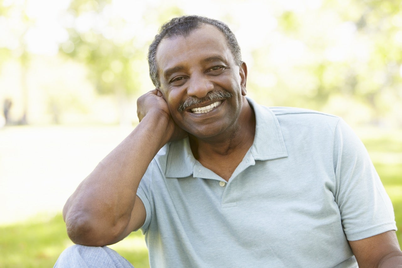 A senior man sits outside and smiles. 