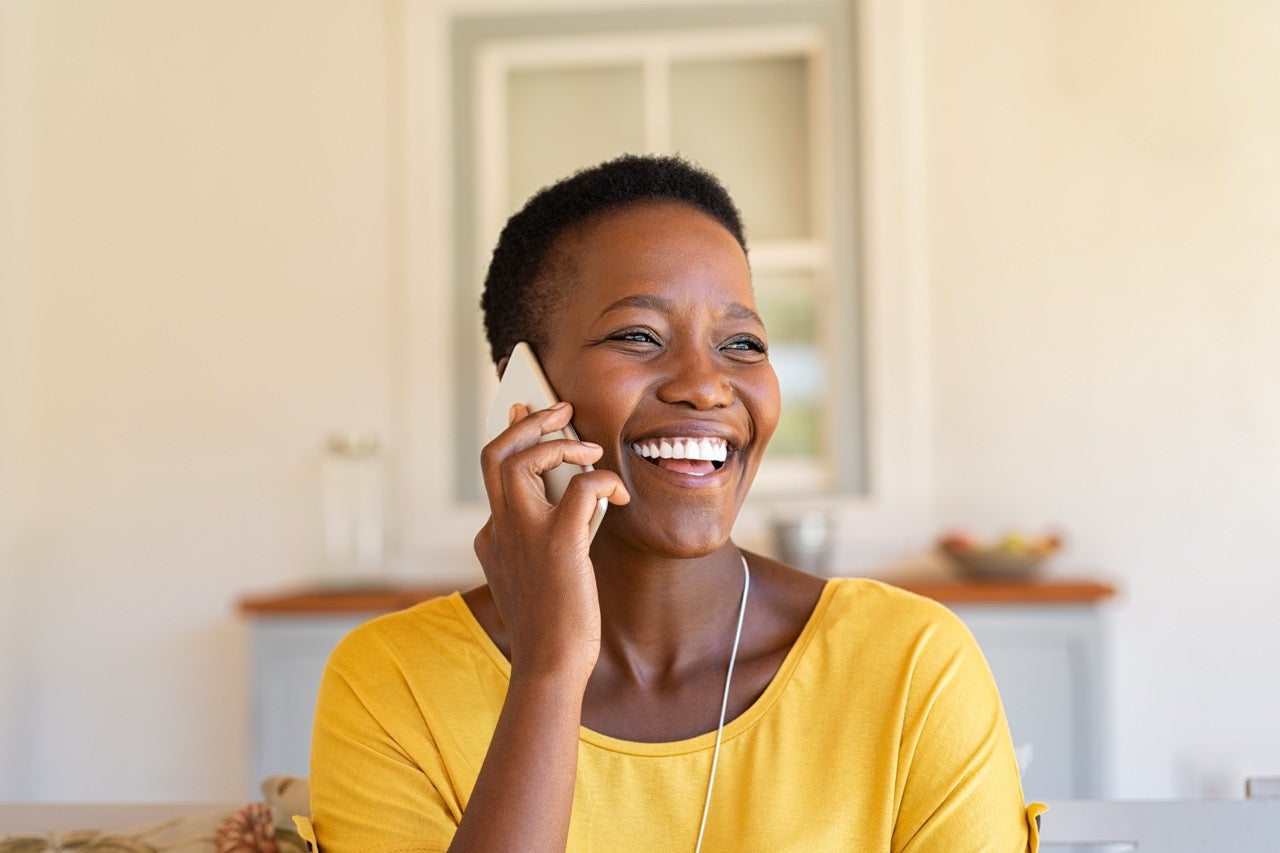 A woman wearing a yellow top smiles as she talks on the phone. 