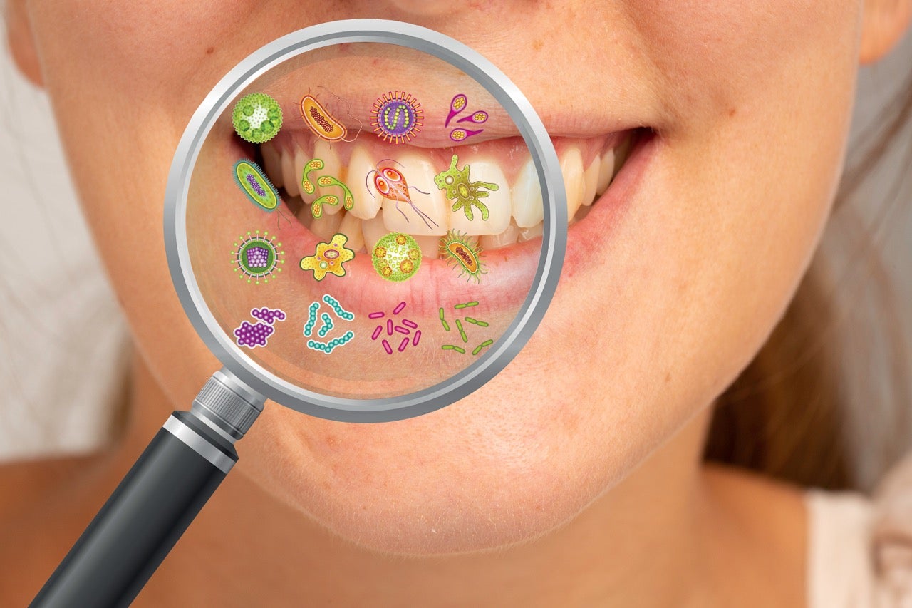 A close-up of a magnifying glass by a young girl’s mouth with colorful bacteria illustrations showing the oral microbiome. 