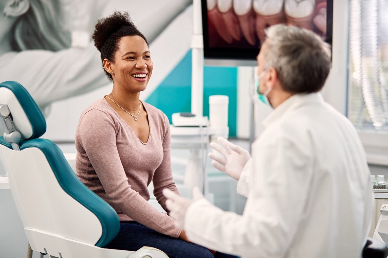 A young woman smiles as she talks to her dentist. 
