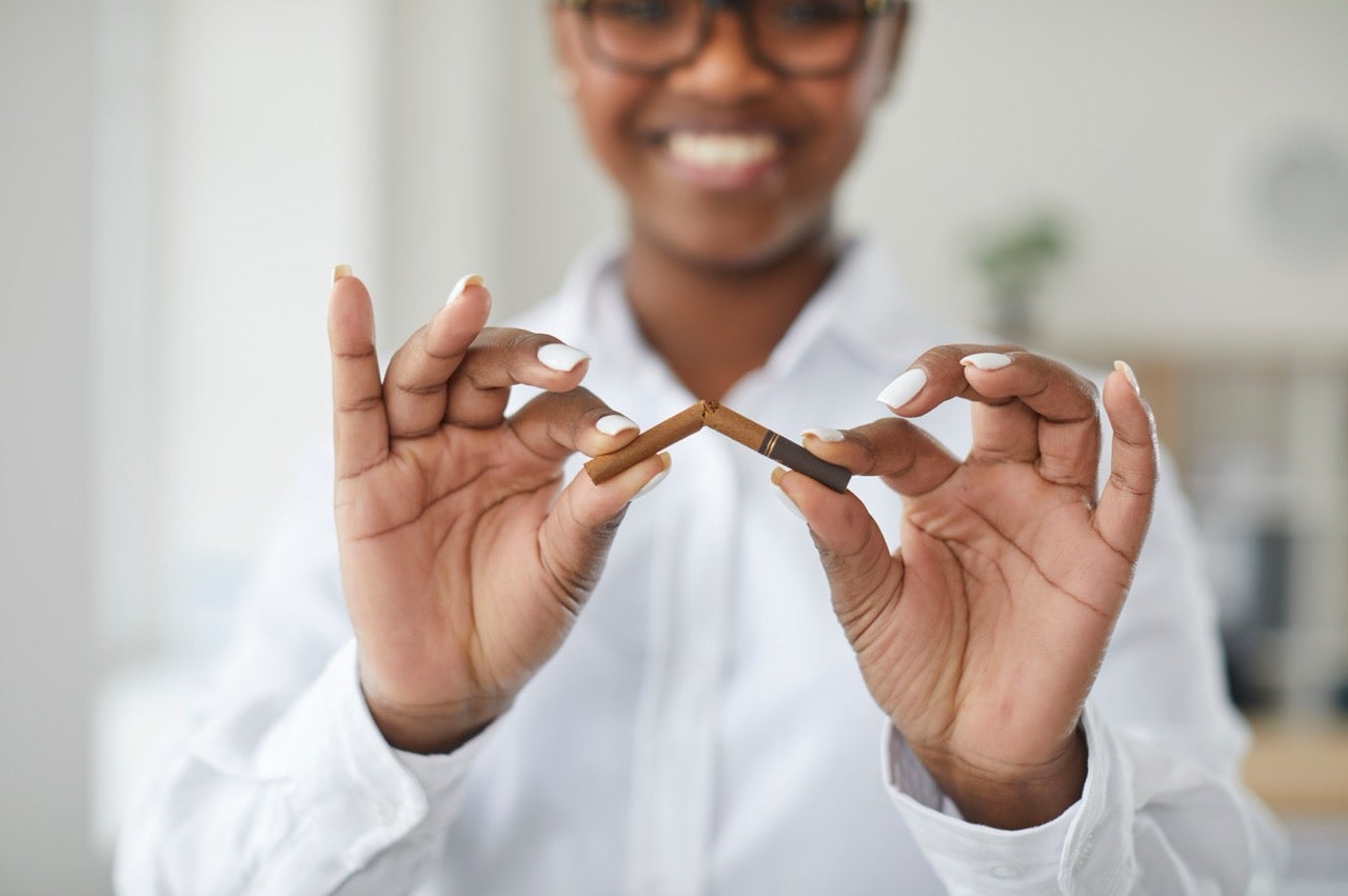 A smiling young woman breaks a cigarette in half because she’s stopping smoking. 