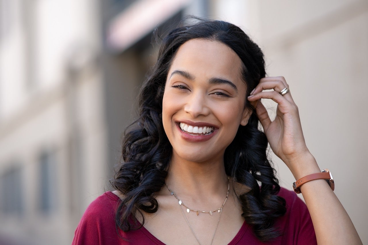 A smiling young woman stands outside. 