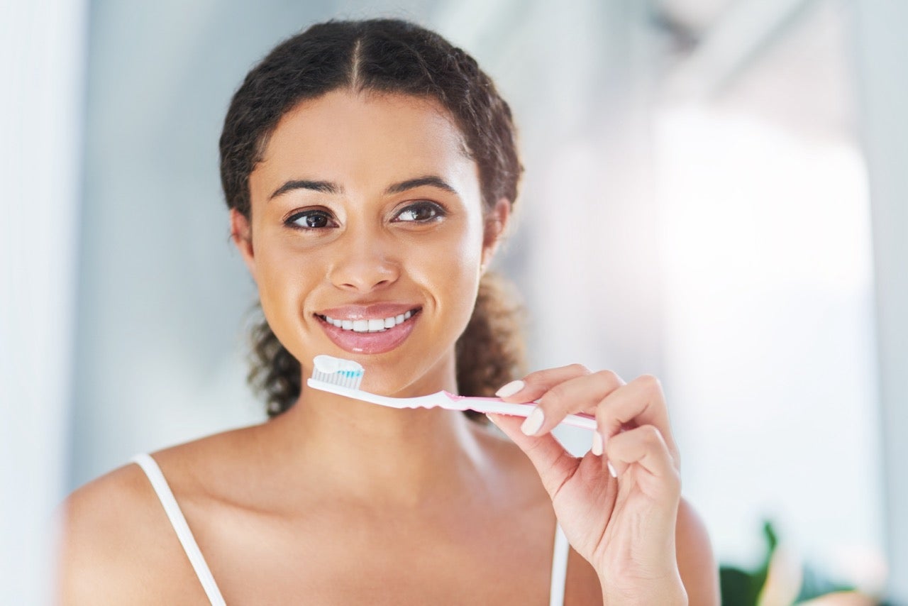 A young woman holds a toothbrush with toothpaste up to her mouth. 