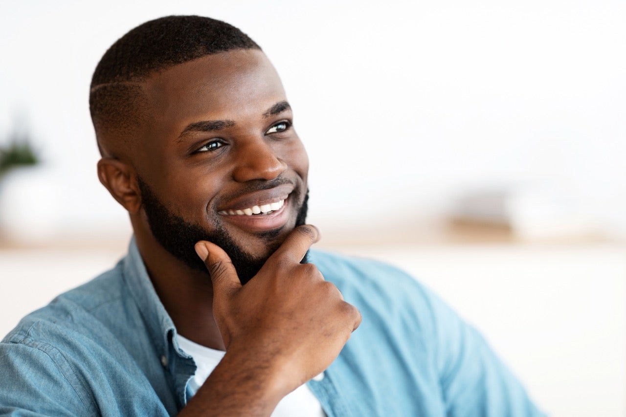 A smiling young man holds his hand up to his chin. 