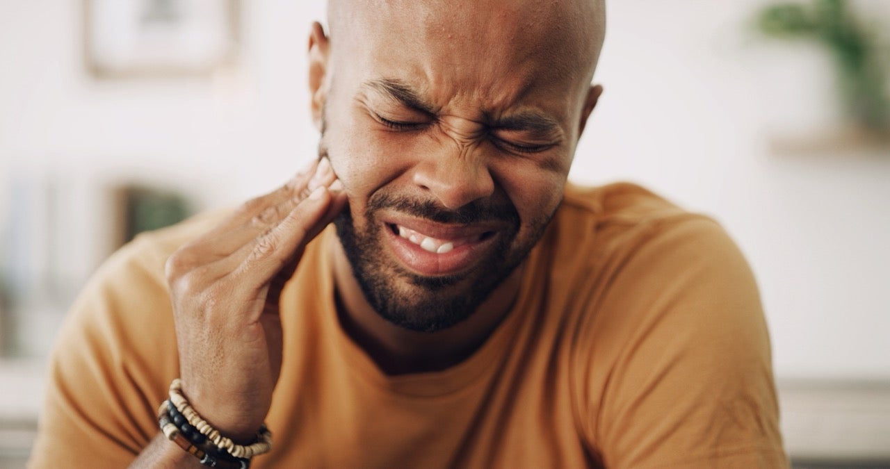 A man suffering from a painful tooth holds his fingers up to his jaw.