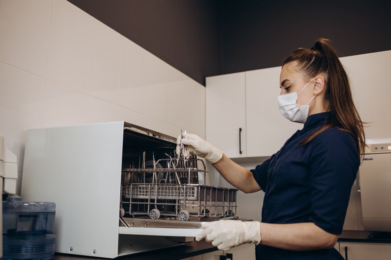 Masked dental assistant loads dental instruments into steam sterilizer.