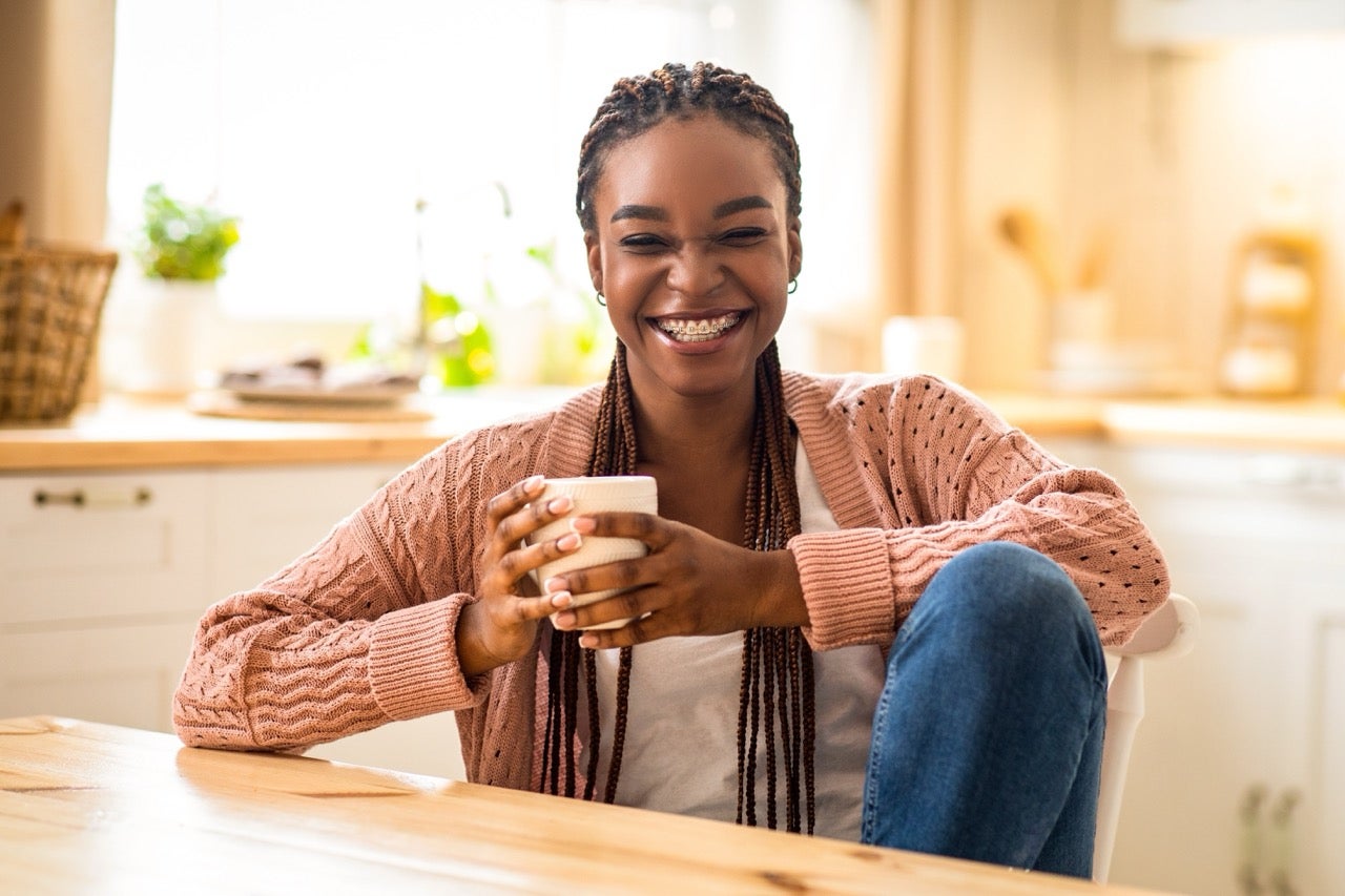 A young woman holds a coffee mug and smiles because she no longer suffers from TMJ.
